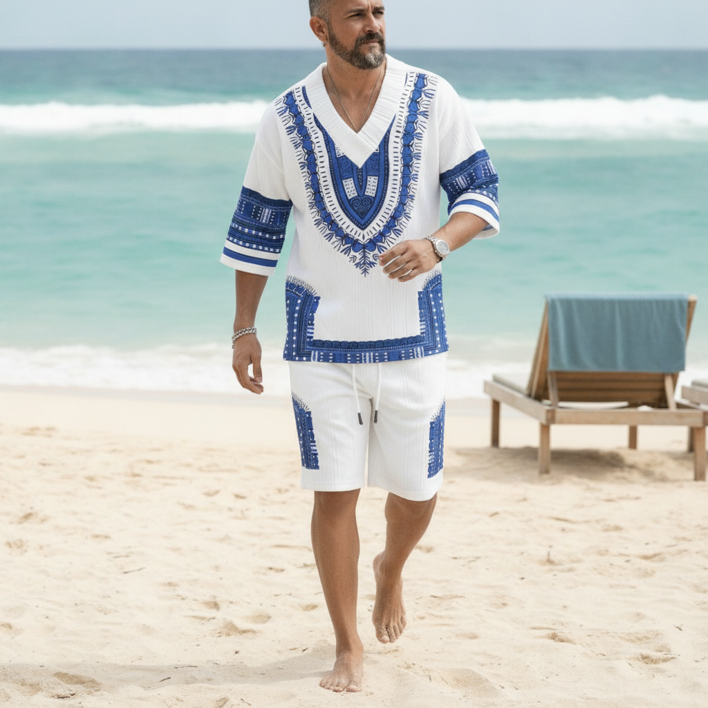 A man in a printed V-neck top and matching shorts walks on a sunny beach, exuding confident vacation style.